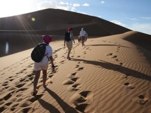 Three people walking across a sand dune in the desert.