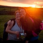 Two ladies pictured in green fields in front of a sunrise
