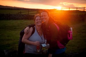 Two ladies pictured in green fields in front of a sunrise