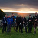 Group of seven people pictured in front of the sun rising over the countryside.