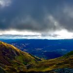 View from the summit of Snowdon looking down the mountain and across the countryside. Features a cloudy sky.