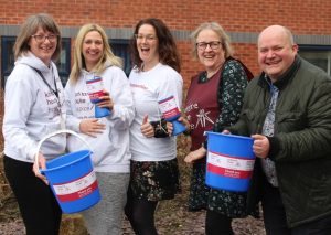 Five smiling members of the Fundraising team at Katharine House Hospice (Stafford) holding donations tins and buckets.