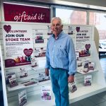 A Katharine House Hospice shop volunteer standing infront of a volunteer display in the Stoke Big Charity Store.