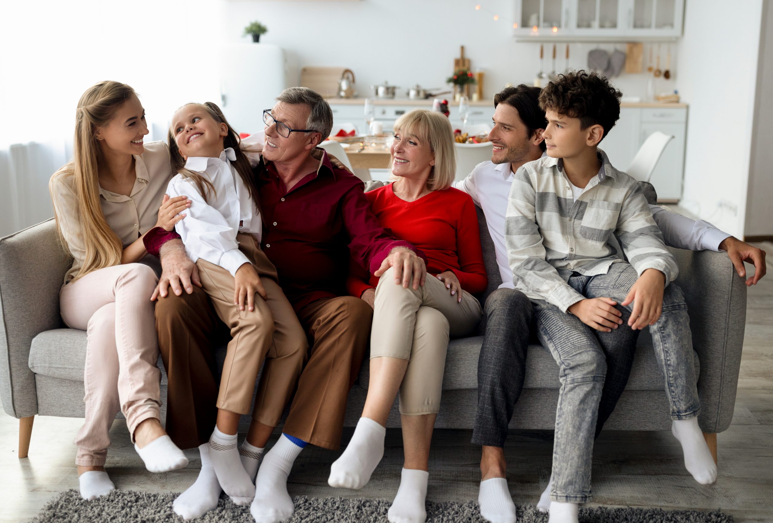 Big multi generation family with kids relaxing on sofa, smiling and chatting, spending bonding times together at home A family of multiple generations gathered on the sofa.