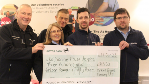 People dressed in work uniform and holding up a giant cheque made out to Katharine House Hospice.