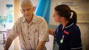 Nurse with hand placed on the back of a standing patient to offer support.