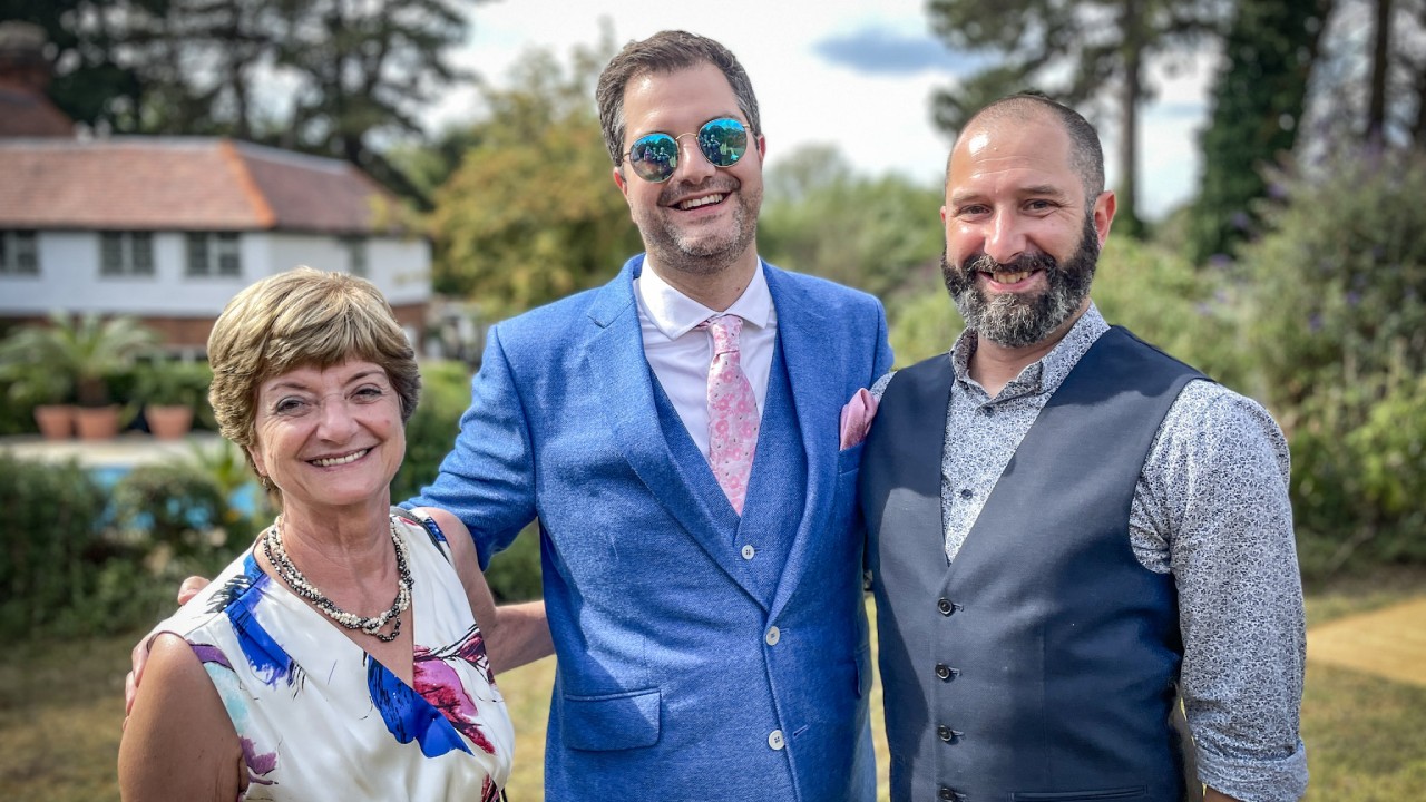 Dr Bernadette Sharp and her sons, Tim and Dan, smiling at the camera on a sunny day.