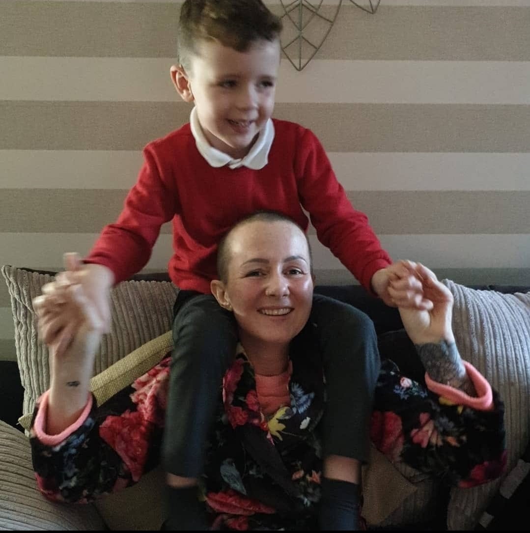 Amy Hollinshead smiling with no hair and her son Darnell when younger on her shoulders