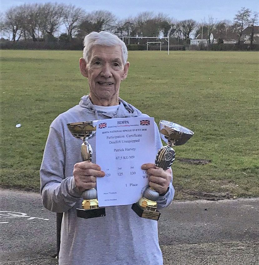 Pat Harvey smiling, holding up his weight lifting trophies