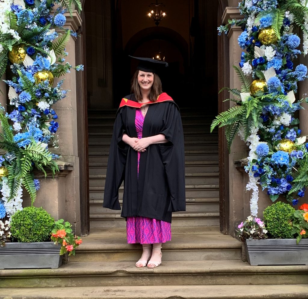 Hospice Lead Nurse Carina Lowe standing under a flower arch at her graduation in a gown and cap