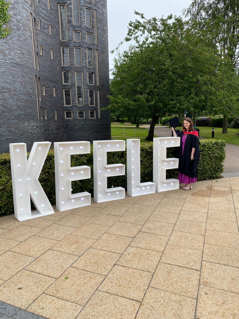 Hospice Lead Nurse Carina Lowe standing next to large lit up letters spelling out Keele at her graduation