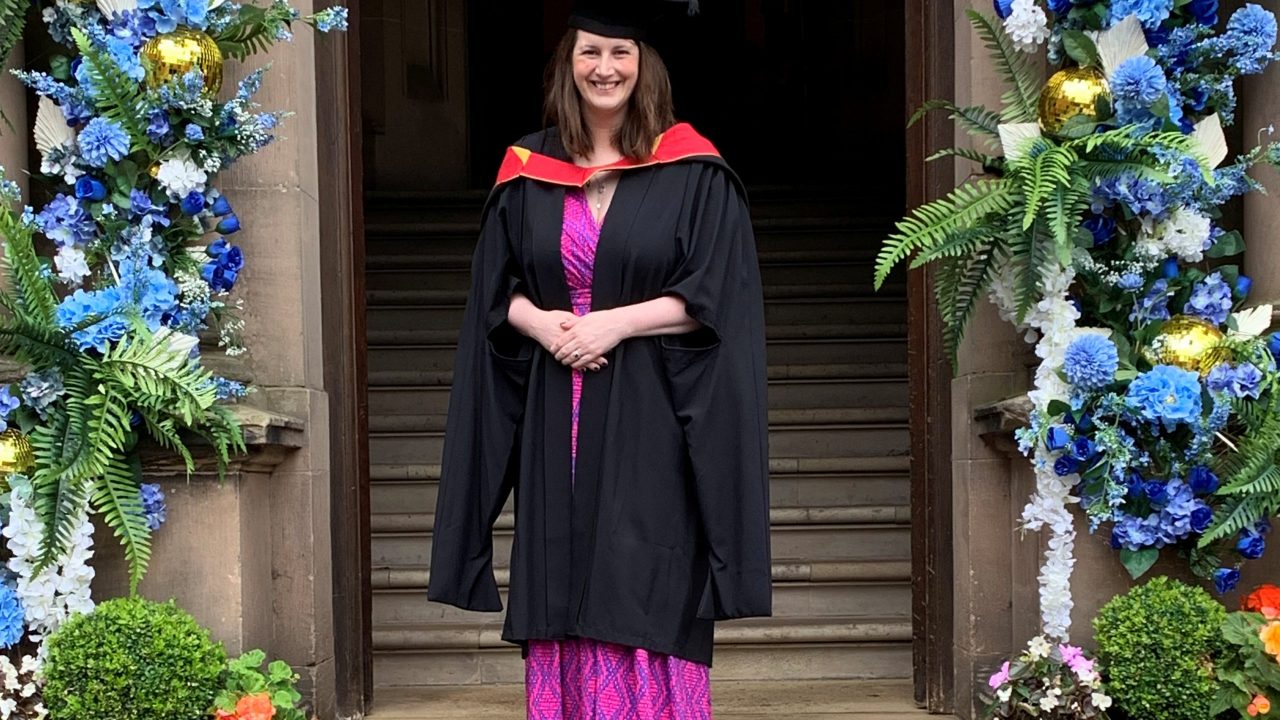 Hospice Lead Nurse Carina Lowe standing under a flower arch at her graduation in a gown and cap