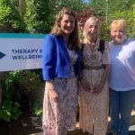 Stafford MP Theo Clarke with Katharine House Hospice patients Alison Buckley and Wendy Bateson smiling in the gardens at the Wellbeing Centre