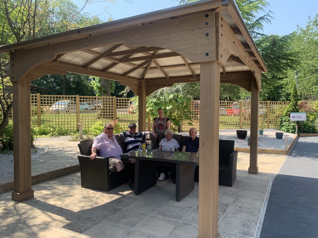Patients sitting and enjoying a drink outside under the gazebo on a summers day.