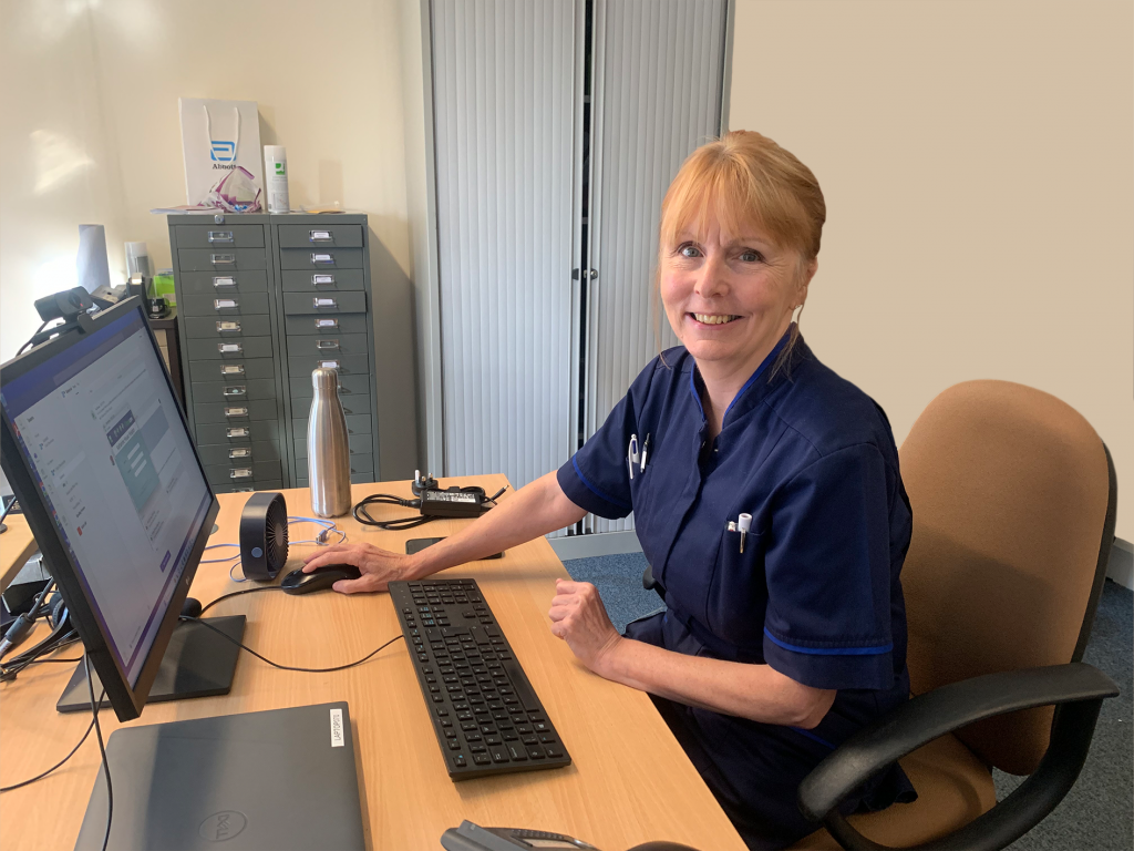 Palliative Nurse Pat sat at her desk and smiling to camera.