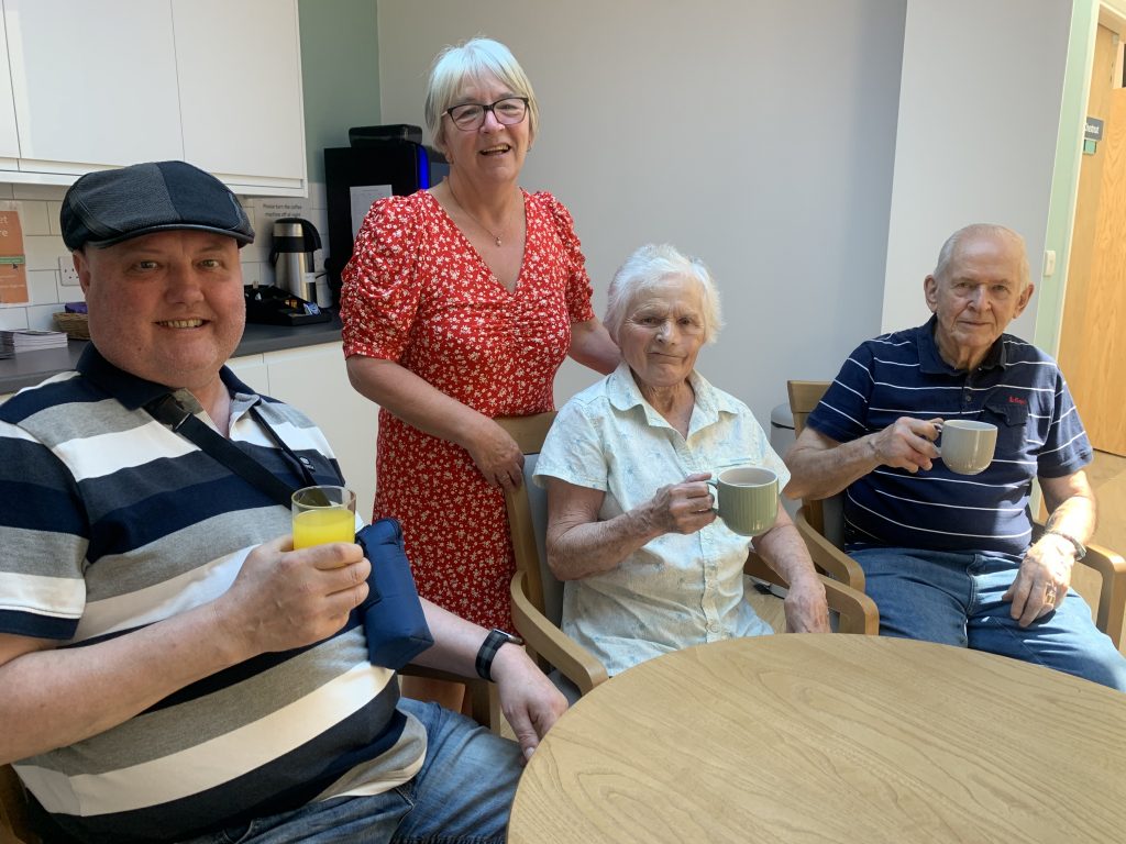 2023_Care_Coffee_Morning_HCA_June_Brammer_with_patients_Alec_Innes_Sylvia_Pollard_&_husband_Roger Patients chatting together around a table