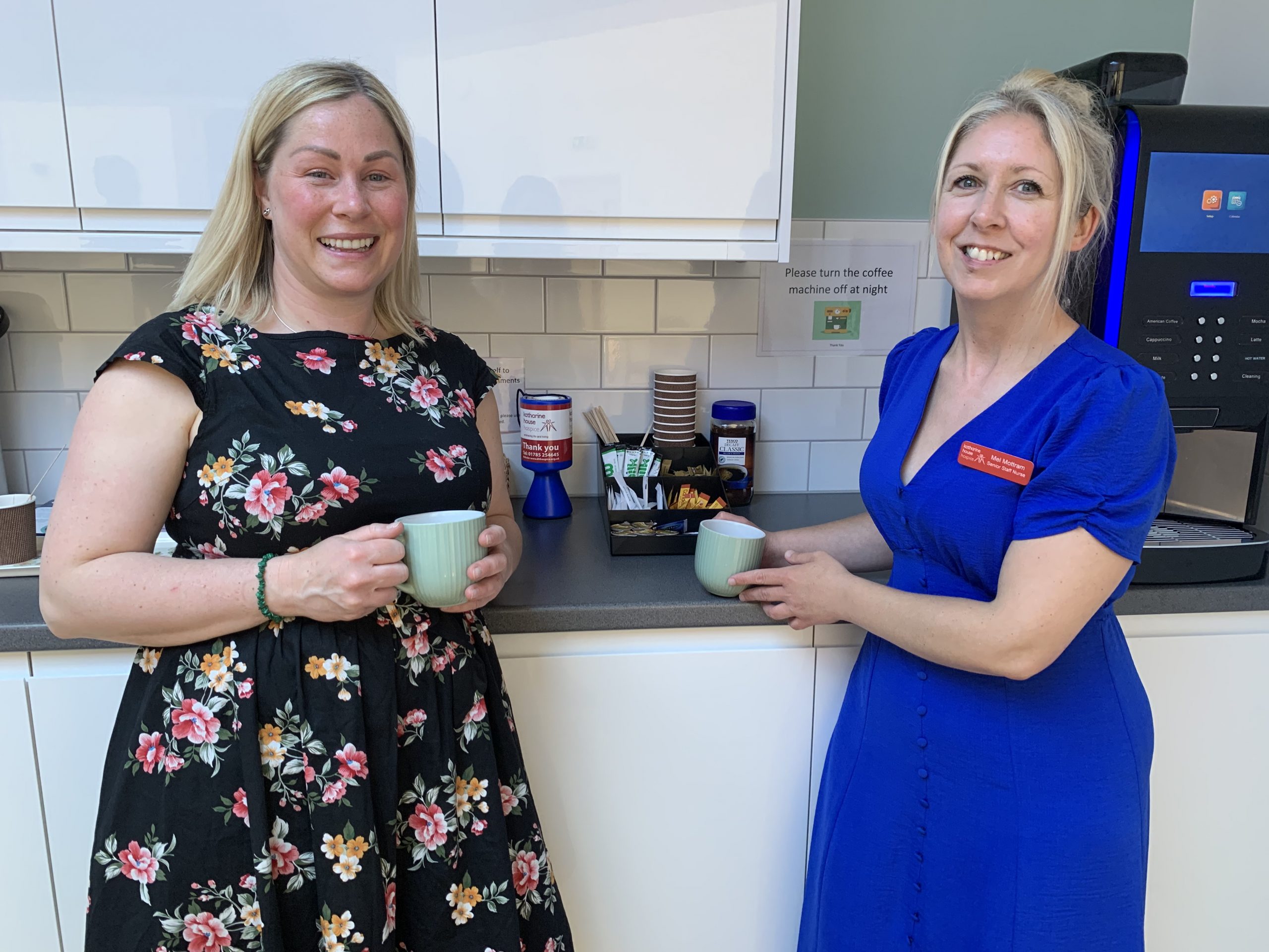 Care nurses Mel and Rachel smile together holding a cup of tea.