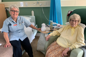 A female healthcare assistant pictured with a seated female patient. Both are smiling. 