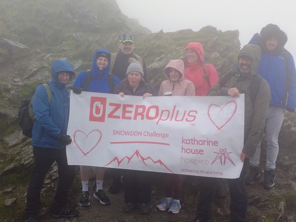 The ZEROplus team smile and hold up a banner showing their support for Katharine House Hospice.