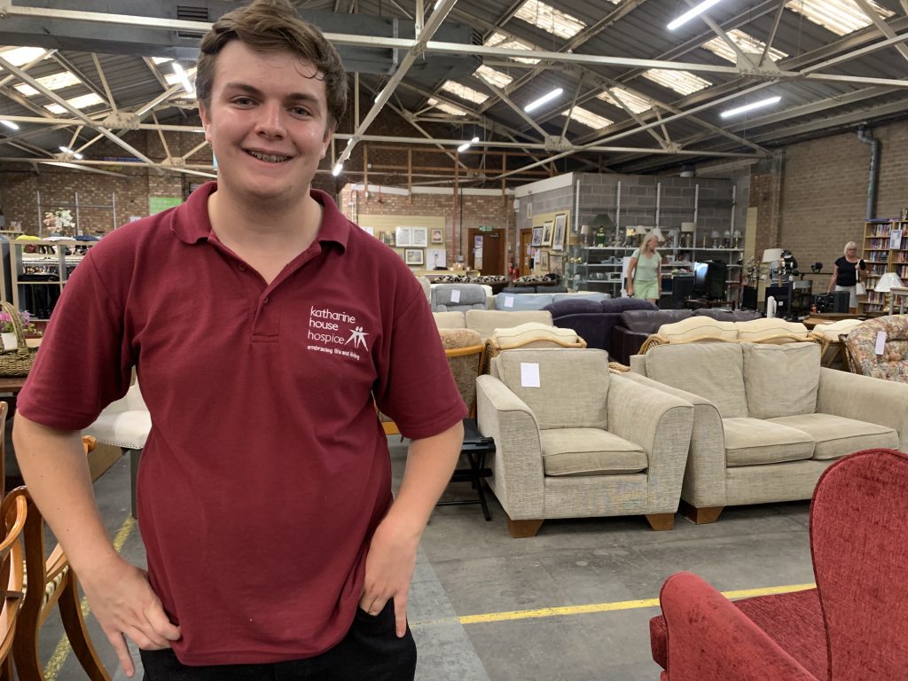Retail volunteer George stands in a warehouse charity shop surrounded by furniture