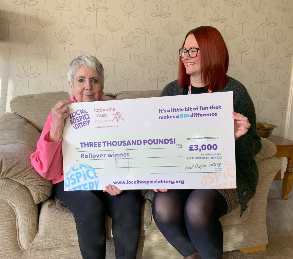 Two women smiling on a sofa with a giant £3,000 cheque