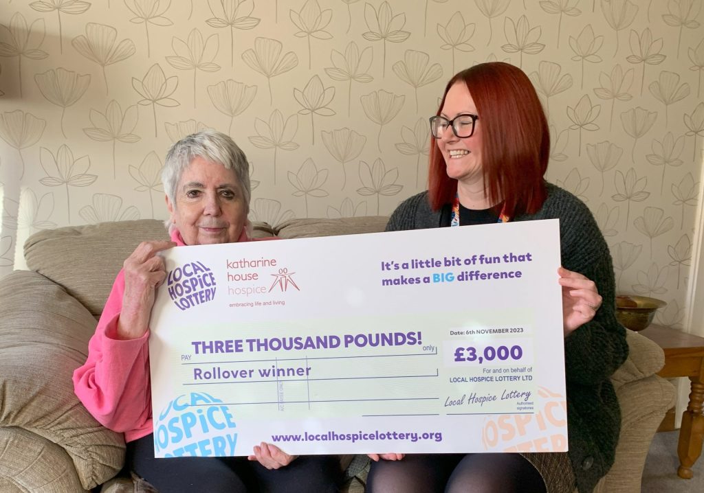 Two women smiling on a sofa with a giant £3,000 cheque