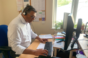Stan from our Patient Pathway team takes a call using a headset and types on the computer keyboard.