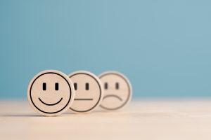 Wooden circles in a line. The unhappy circle is at the back with the happy face in front and in focus.