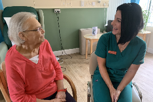 Senior female patient seated beside female medical director; both smiling at one another.