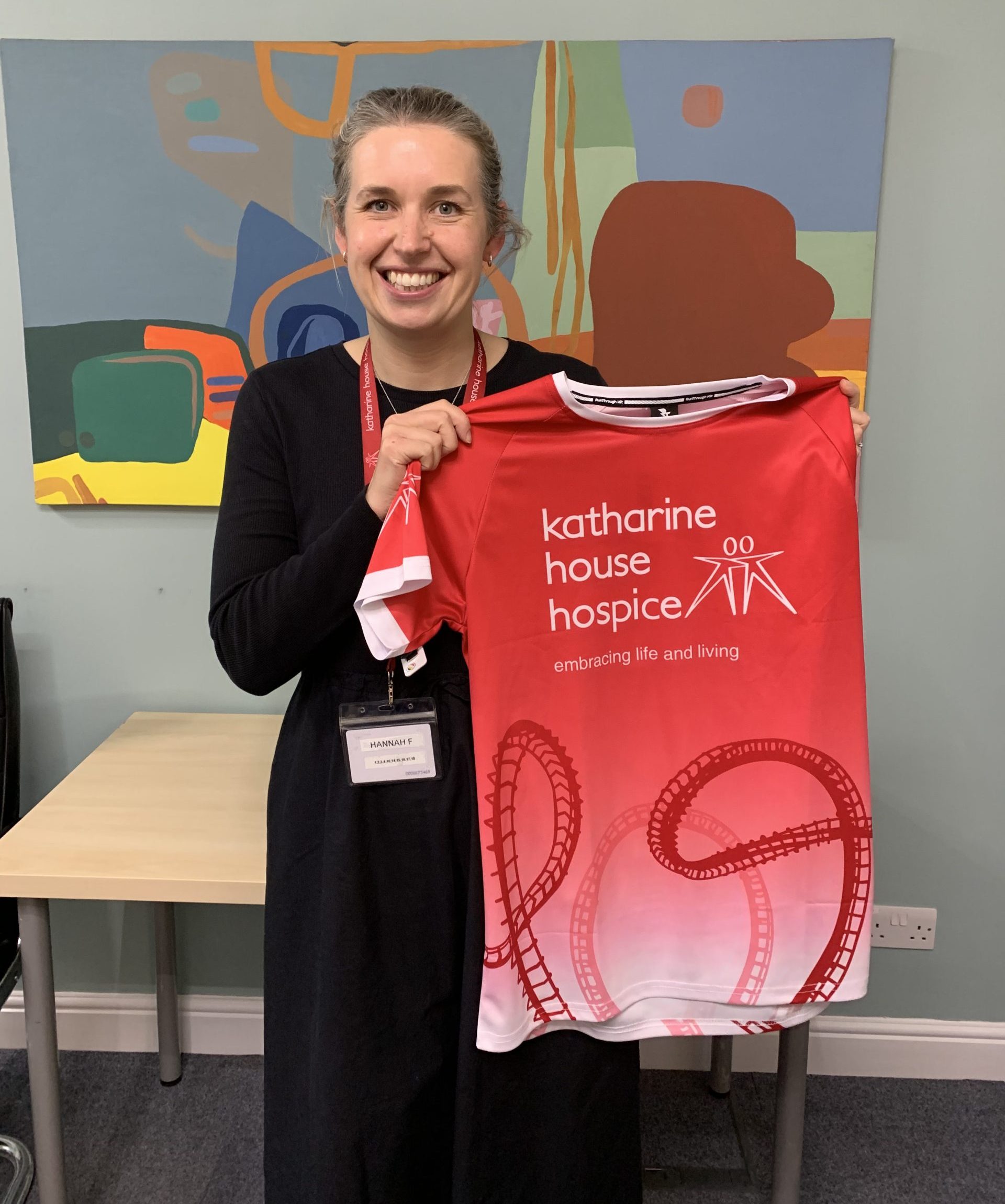 Smiling woman holds a red "Katharine House Hospice x Run Alton Towers" running top.