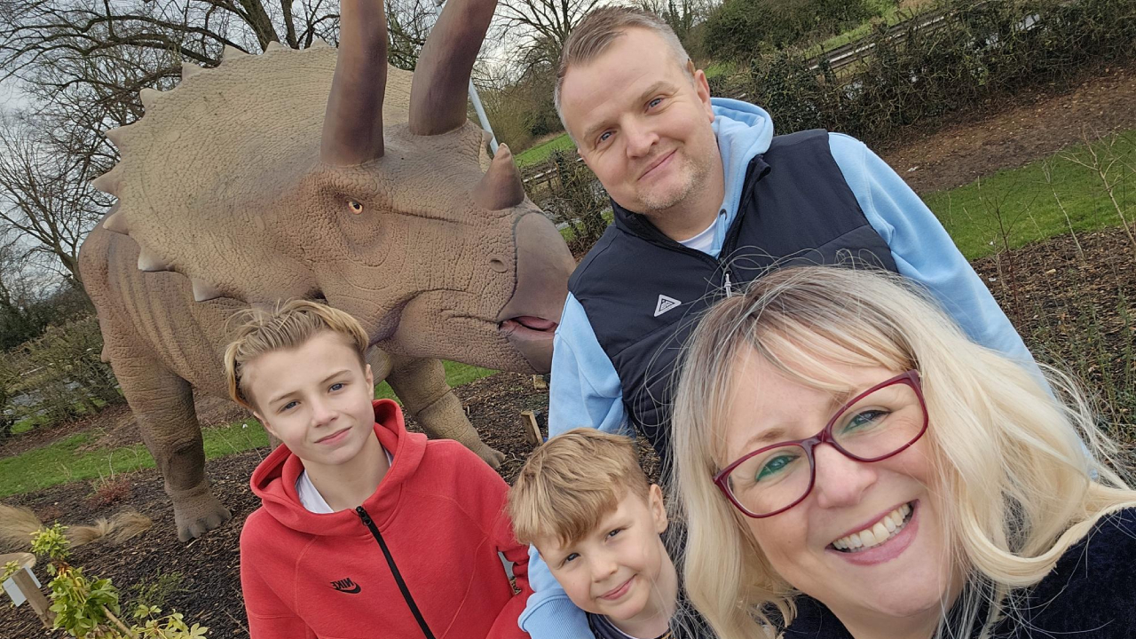 Two sons and their parents smile stood next to a dinosaur statue