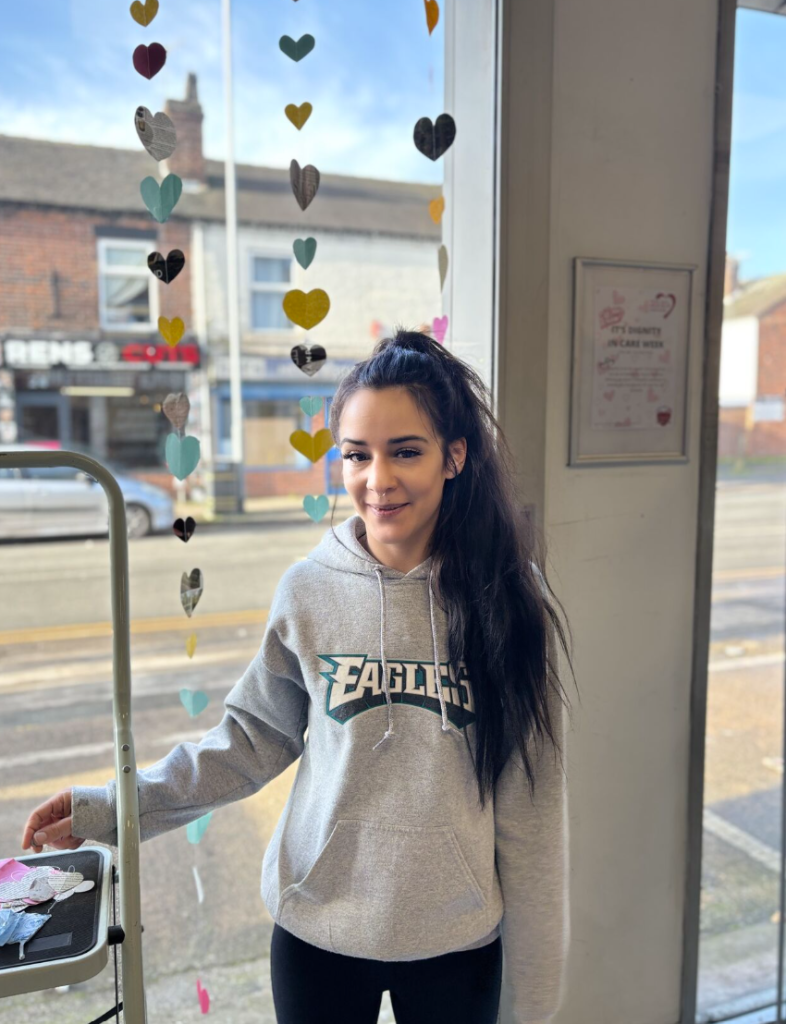 Ellie smiling to camera, in front of the window display she created.