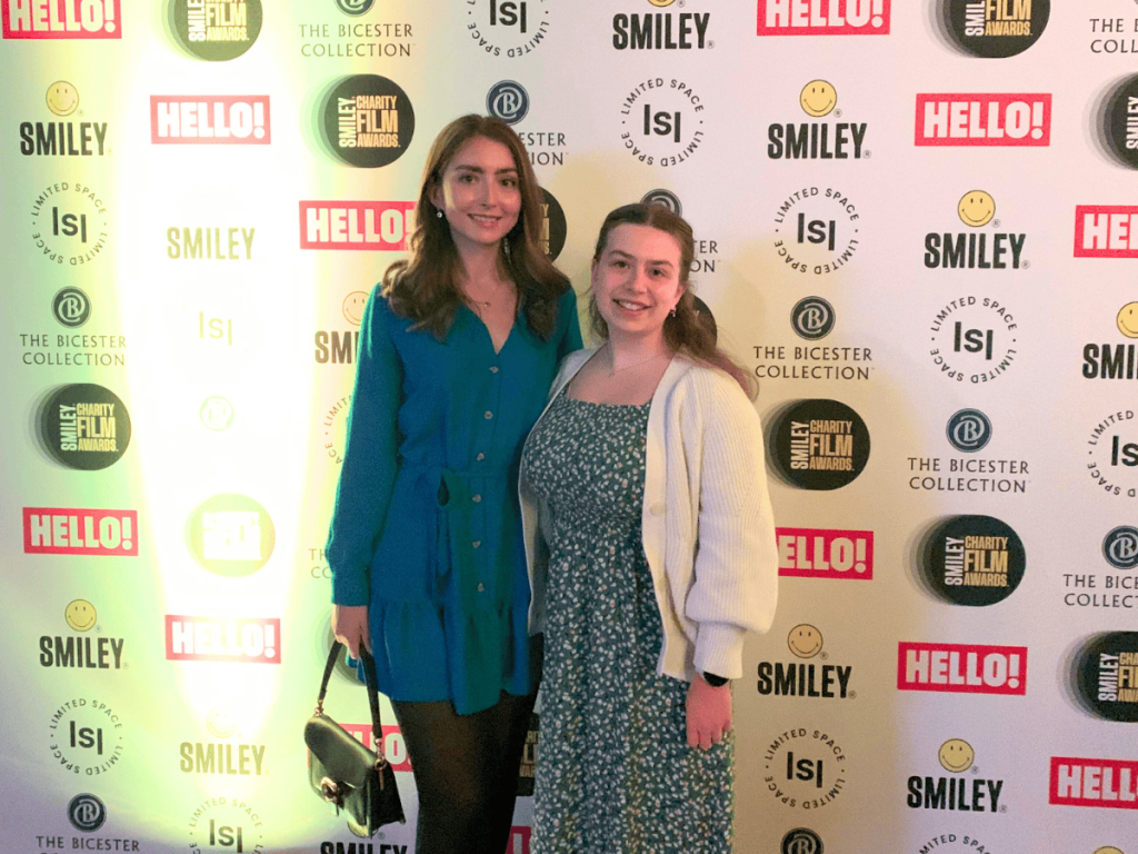 Lydia and Mia have a photo together in front of a Smiley Charity Film Award photo backdrop.
