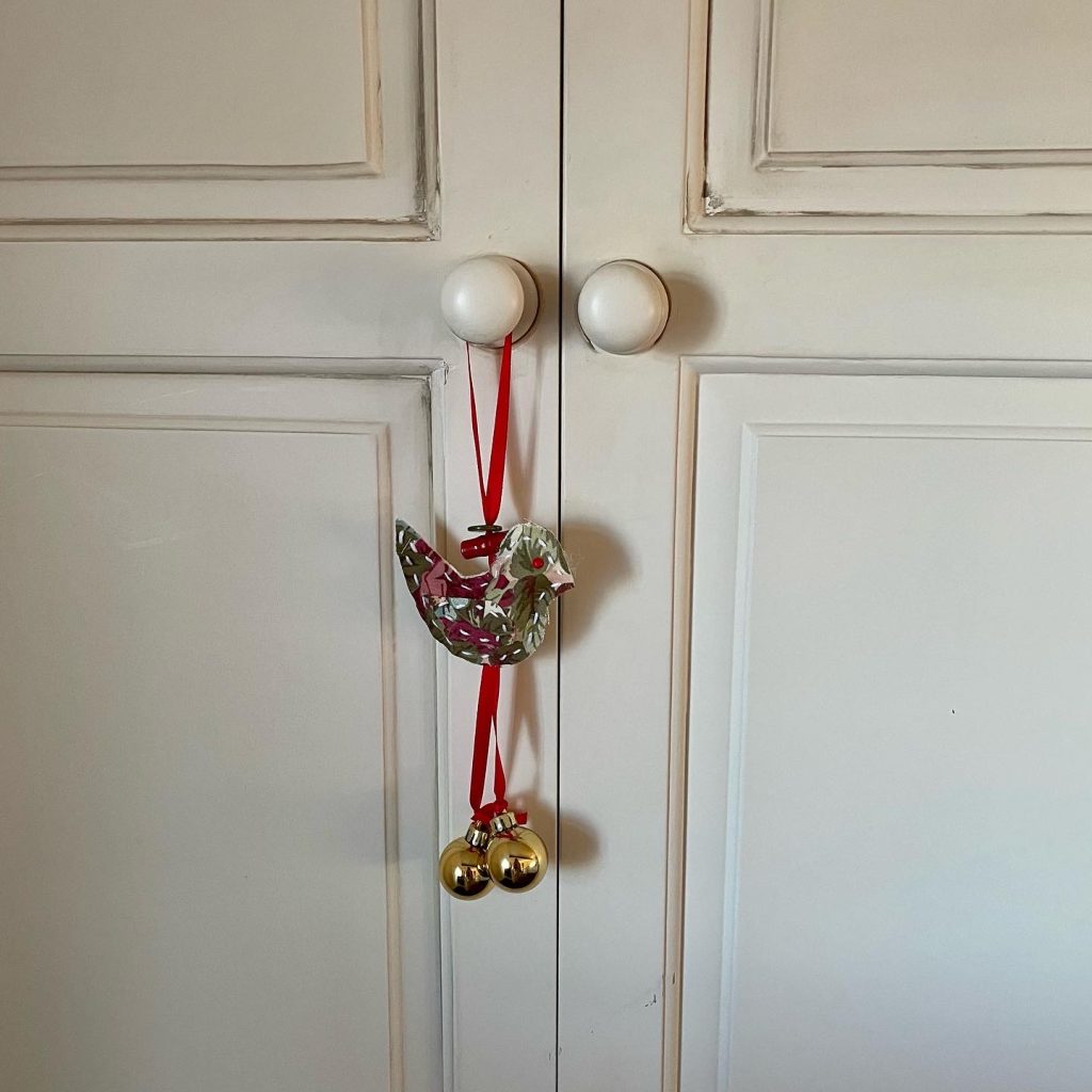A hanging decoration in the shape of a bird made from fabric, and with bells at the bottom. All materials sourced from Katharine House charity shops.