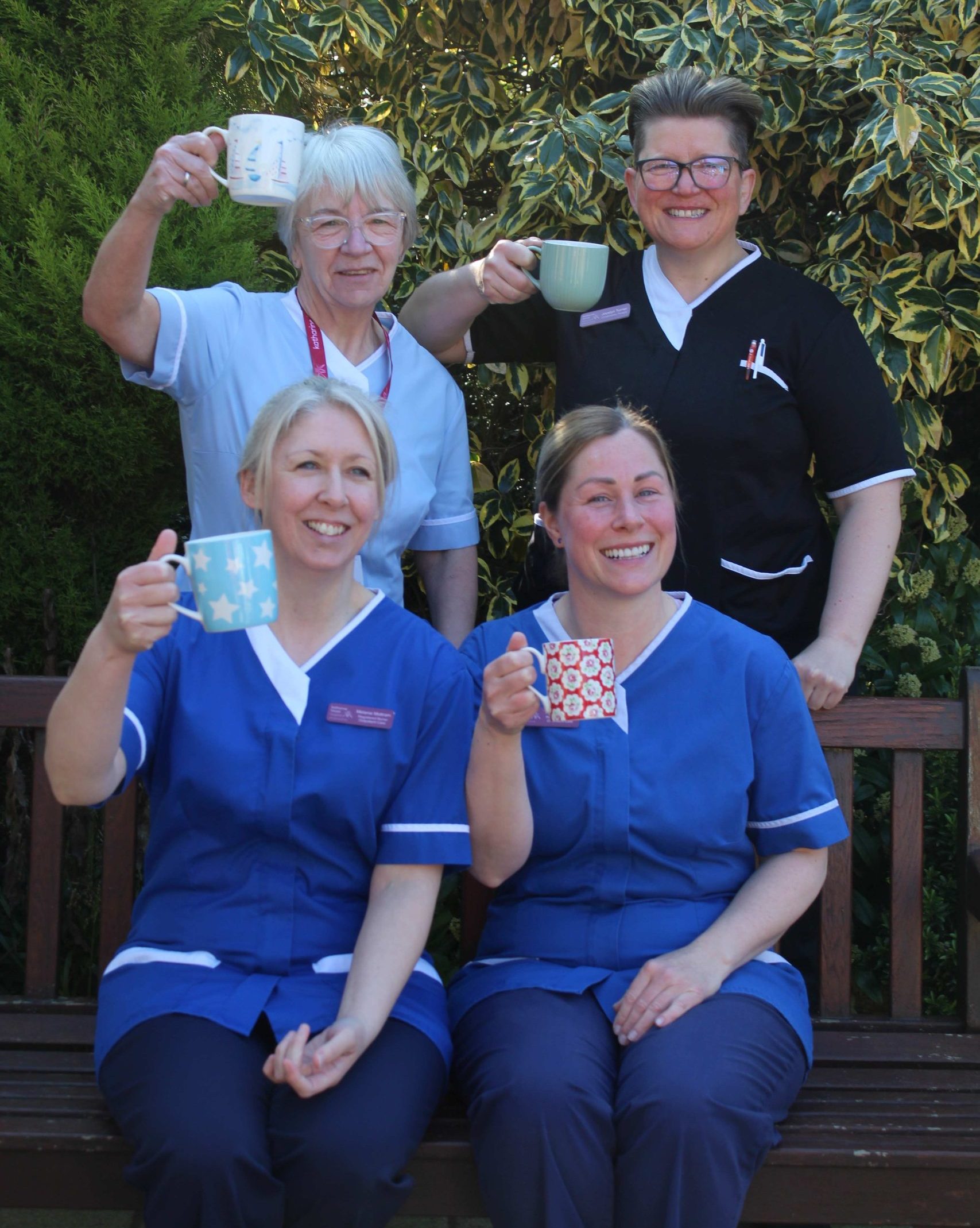 Care for a Cuppa nurses Four female uniformed healthcare workers smiling at the camera and holding up cups of tea.
