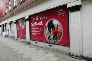 IMG_1558 A large window space filled with a red poster with the words Thank you, Stafford and a picture of a young child being helped on a bike by a man in a hoodie and wellies.