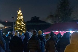 A large Christmas tree lit up with golden lights with a crowd of people standing infront of it in the dark
