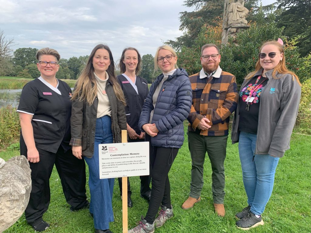 The team stand round one of the prompts at Shugborough, smiling to camera.