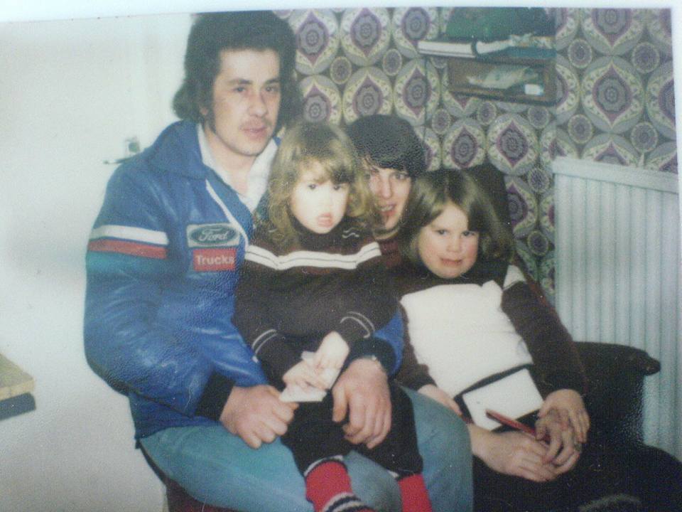 Young couple sitting at home with their two little girls on their knees.
