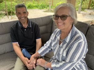 Couple sitting together outside in the sunshine in a garden setting holding hands and smiling