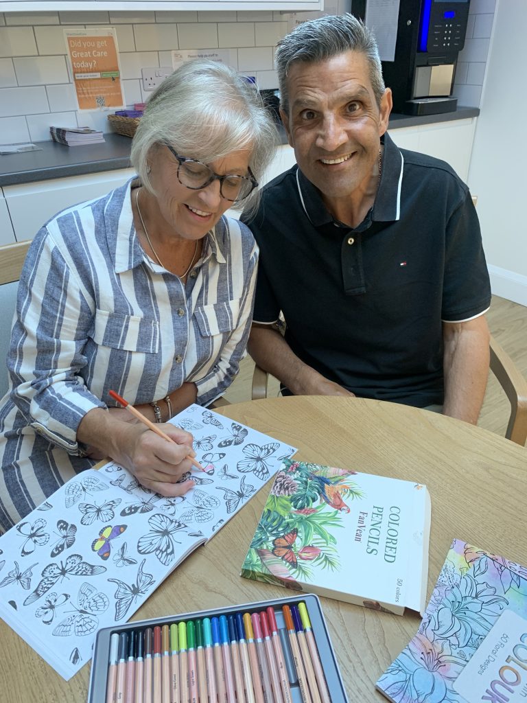 Adrian and Gaynor Niak (25) Couple sitting together at a table, smiling and completing mindful colouring.