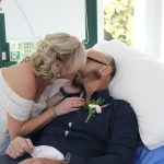 A blonde lady in wedding dress kissing a man in a dark shirt.