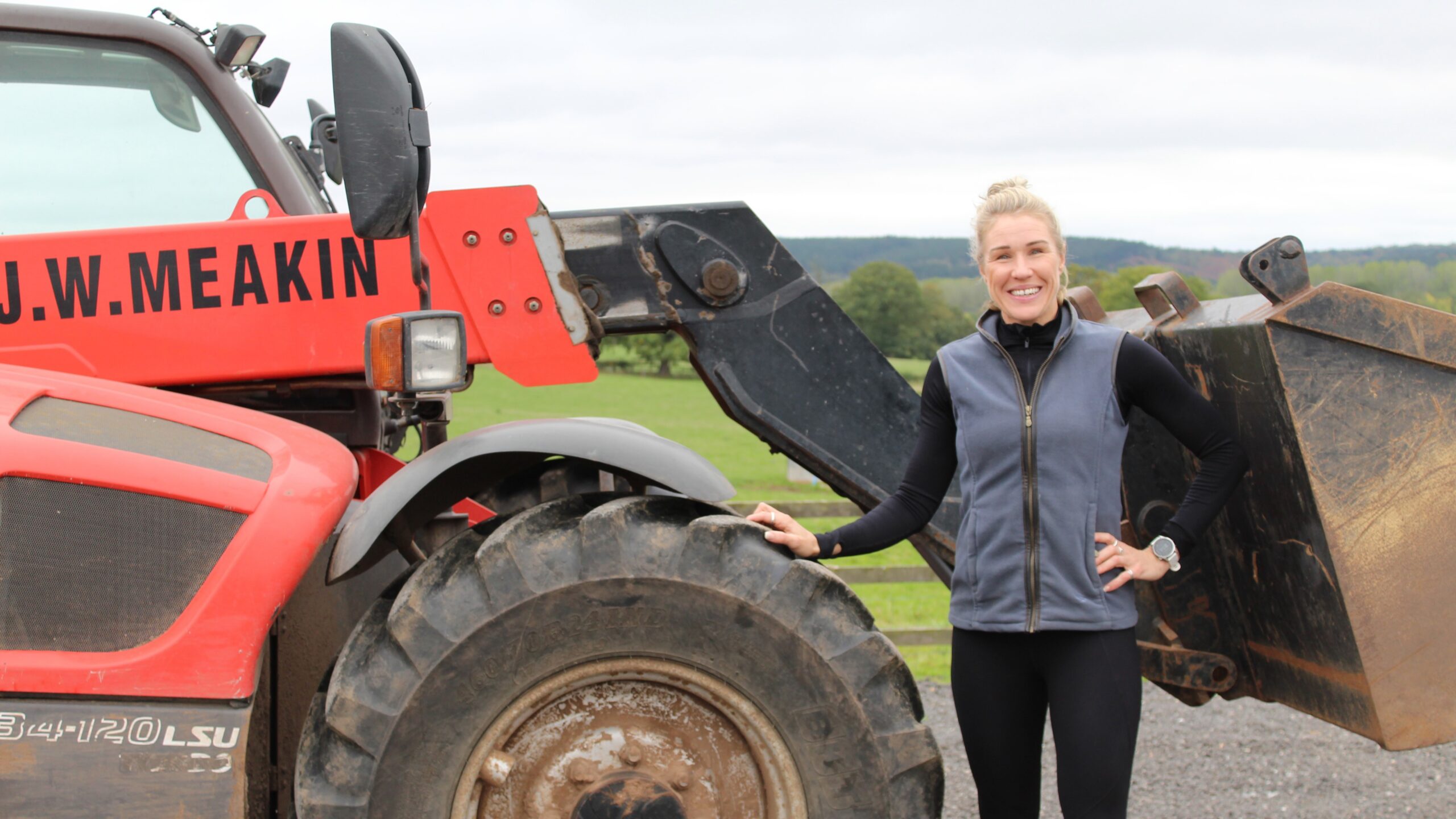 Emily standing by a red tractor with her dad's name on it.