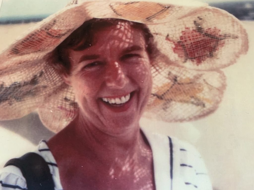 A pretty lady in a wide brimmed sun hat in a holiday setting, smiling.