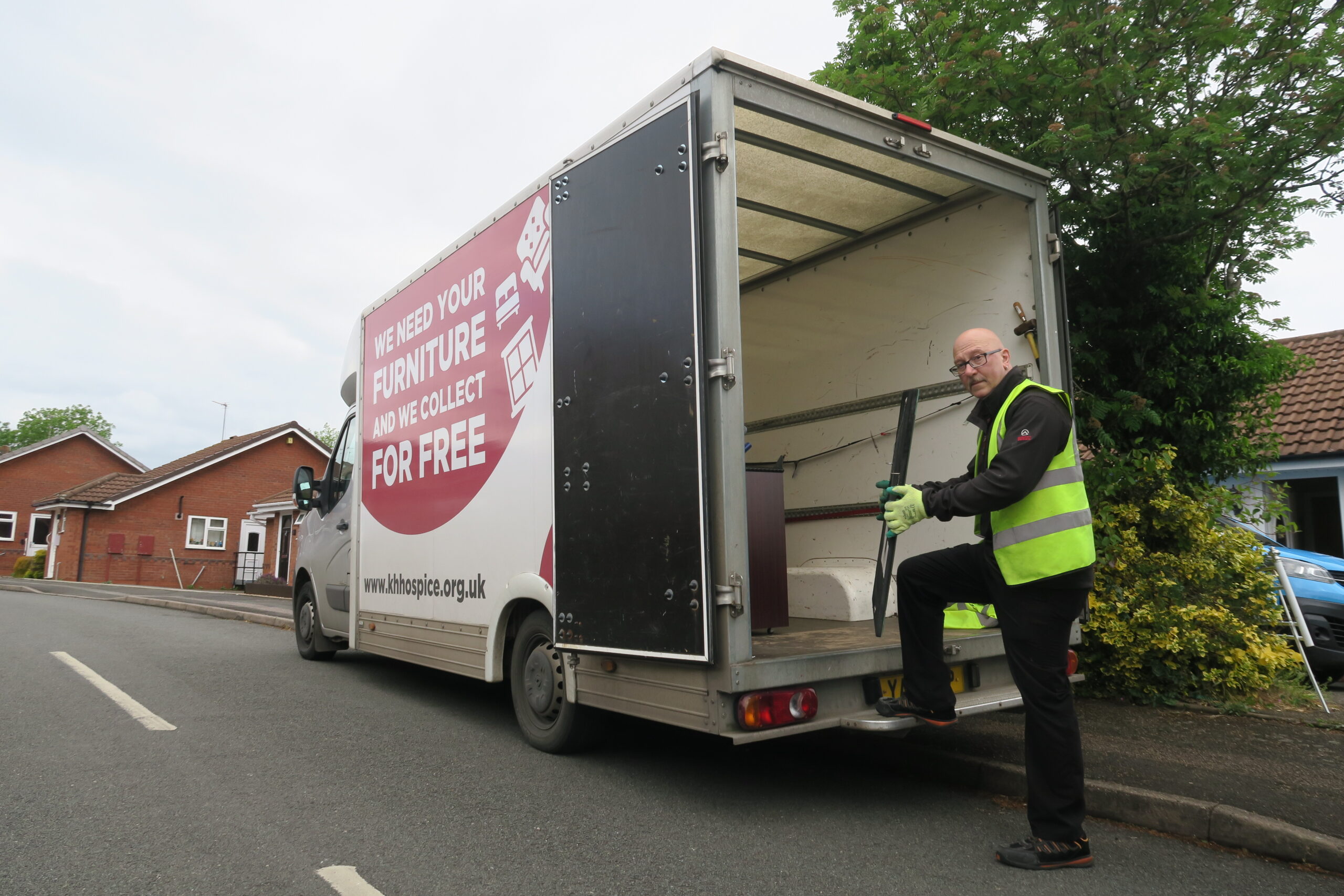 A man wearing a hi-vis waistcoat, putting a piece of furniture into a van