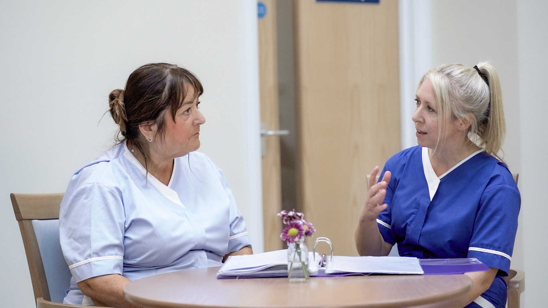 Two nurses chatting, looking through a document together.