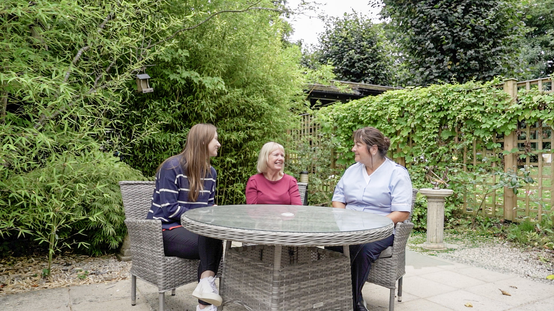Three people sat outside around a table, talking to each other.