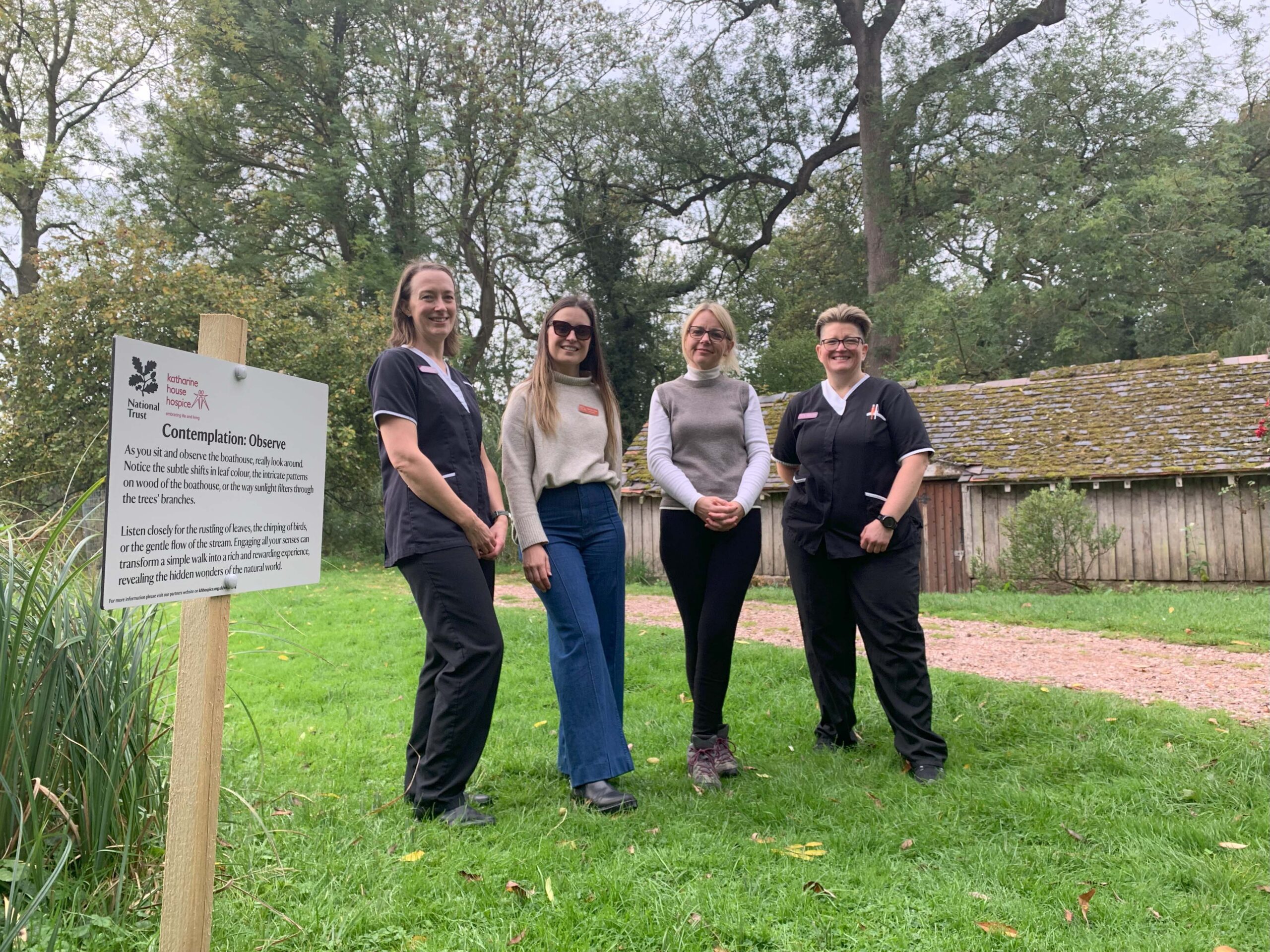 Four people standing by a wooden stake which is titled 'Contemplation: observe' and encourages people to take in their surroundings and be present.