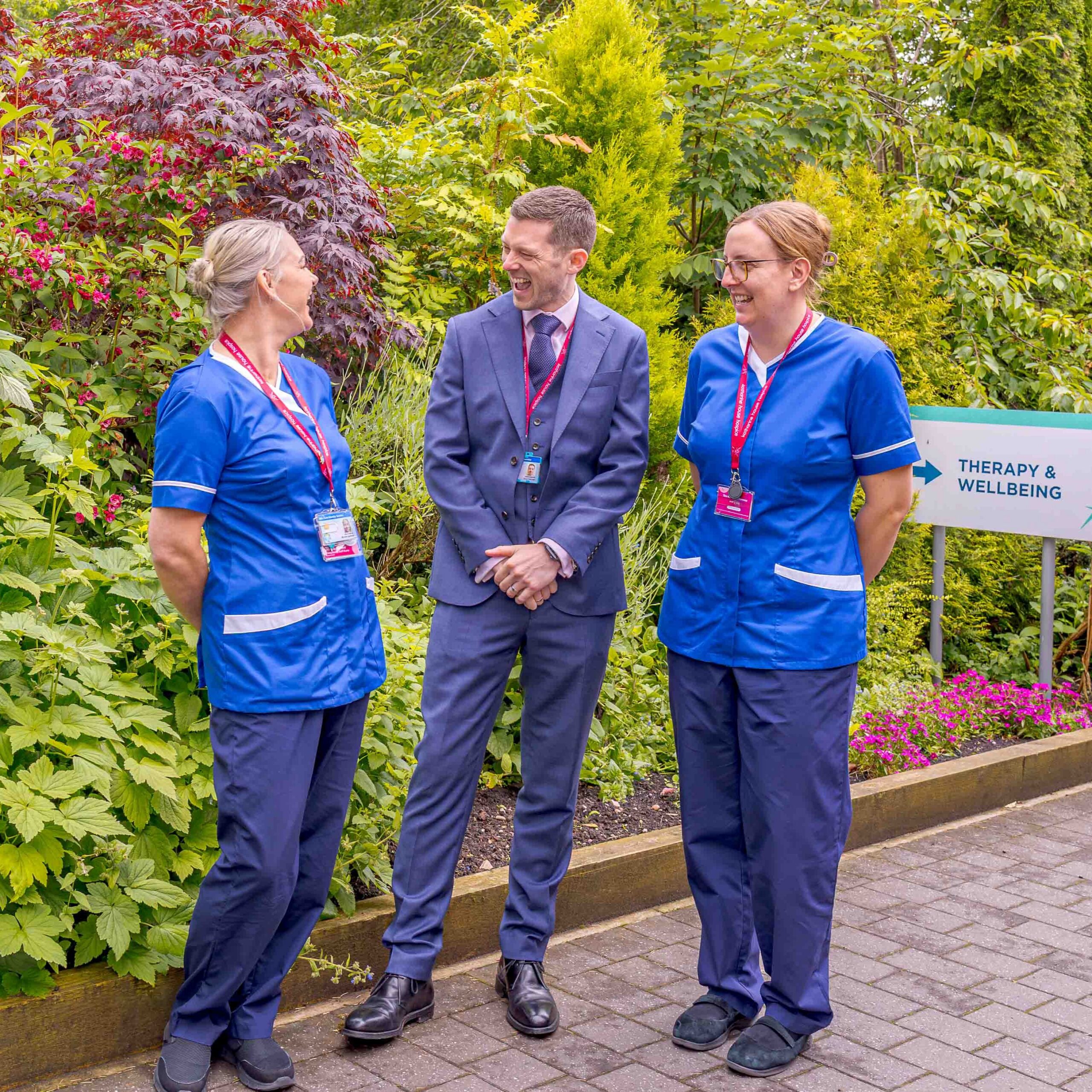 Three people stand smiling in a lush garden near 
