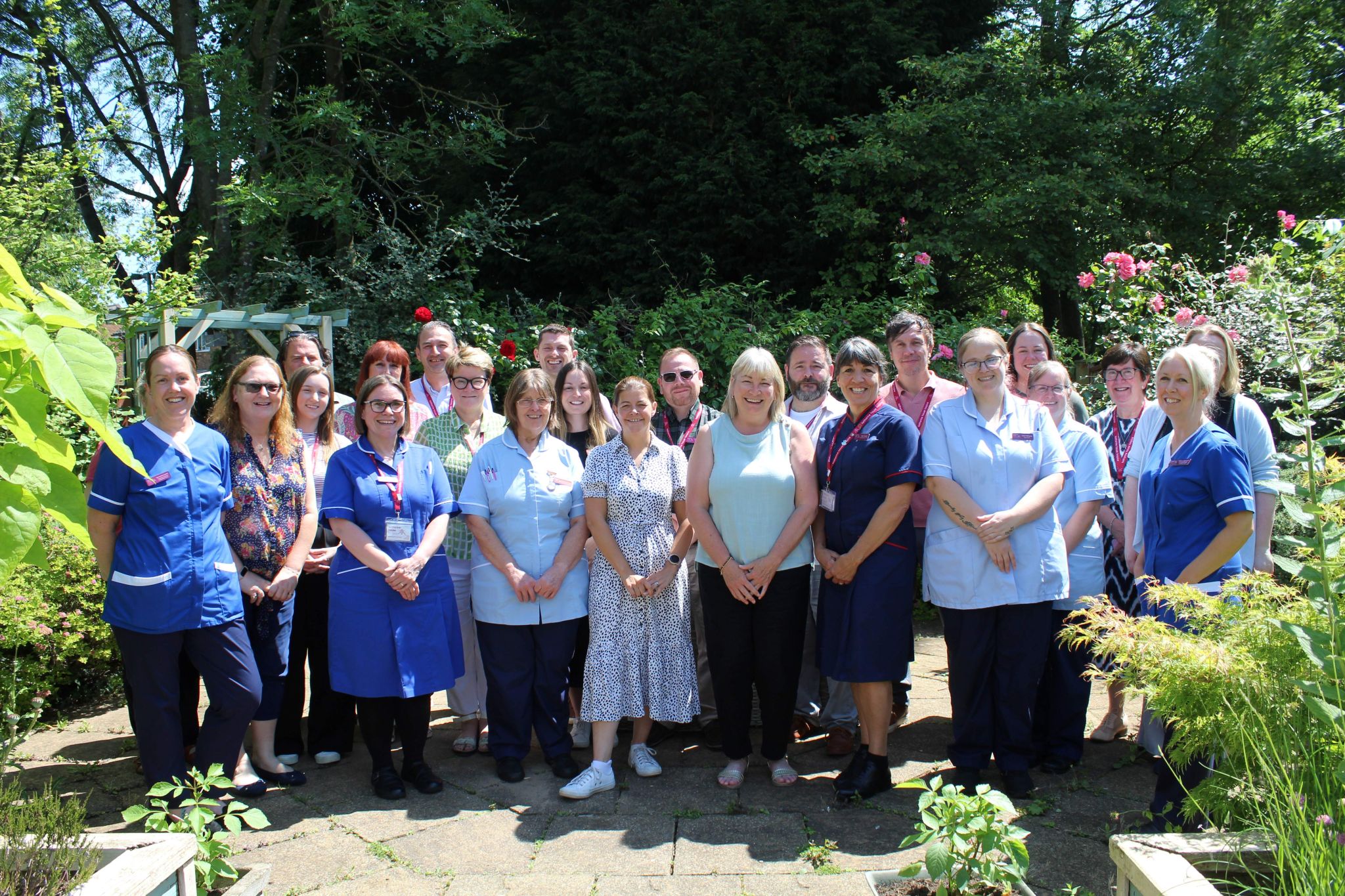 A group of care staff stand together in the hospice garden, smiling at the camera.